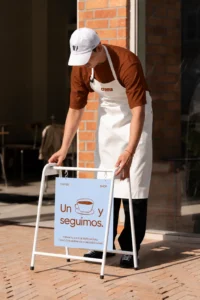 Empleado de Crema Café colocando el caballete de la cafetería con el cartel «Un café y seguimos»